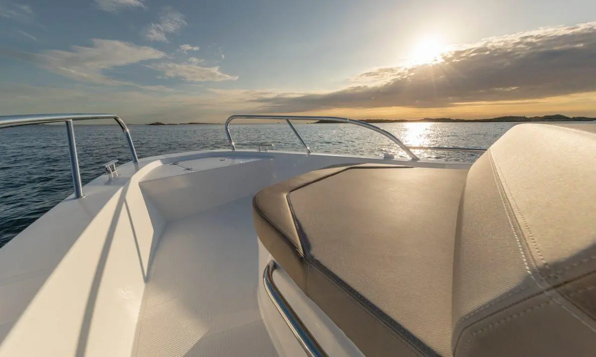 A serene view from a boat's seating area, overlooking calm waters at sunset, with sunlight reflecting on the water's surface.